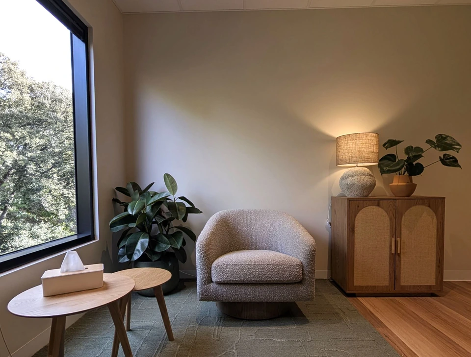 An armchair, leafy window, plants and a warm lamp in Michelle’s therapy room.